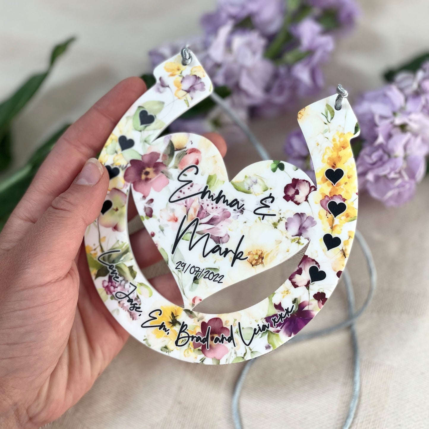 Floral horseshoe design with engraved names being held up by hands with a floral background angled shot