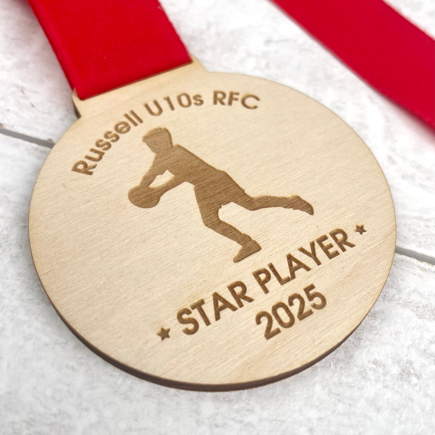 Wooden eco-friendly rugby medal with 'Russell U10s RFC' and 'Star Player 2025' engraving with a red ribbon.