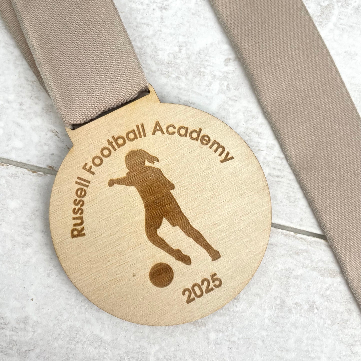 Wooden medal with 'Russell Football Academy' and '2025' engraved.