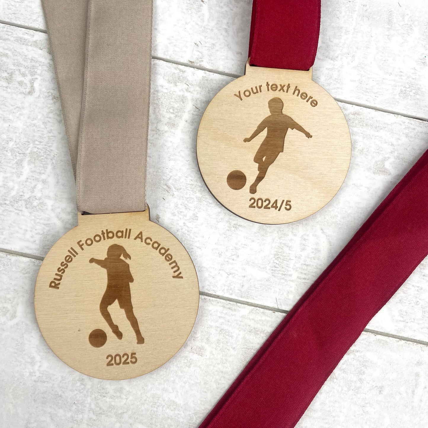 Two wooden medals with engraved silhouettes of a football player and text 'Russell Football Academy 2025'
