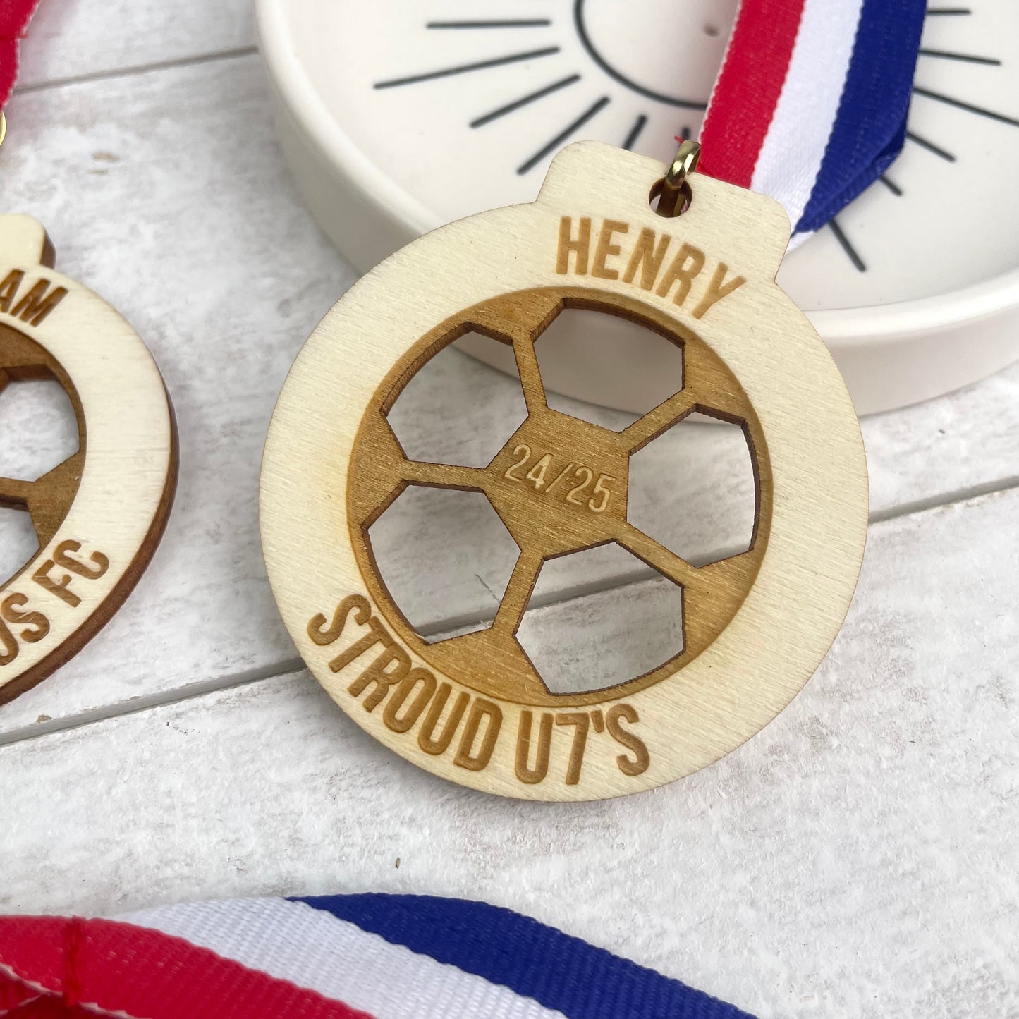 Wooden medal with engraved text 'Henry' at the top '24/25' in the centre and 'stroud u7's' at the bottom. This comes with a striped blue, white and red ribbon.