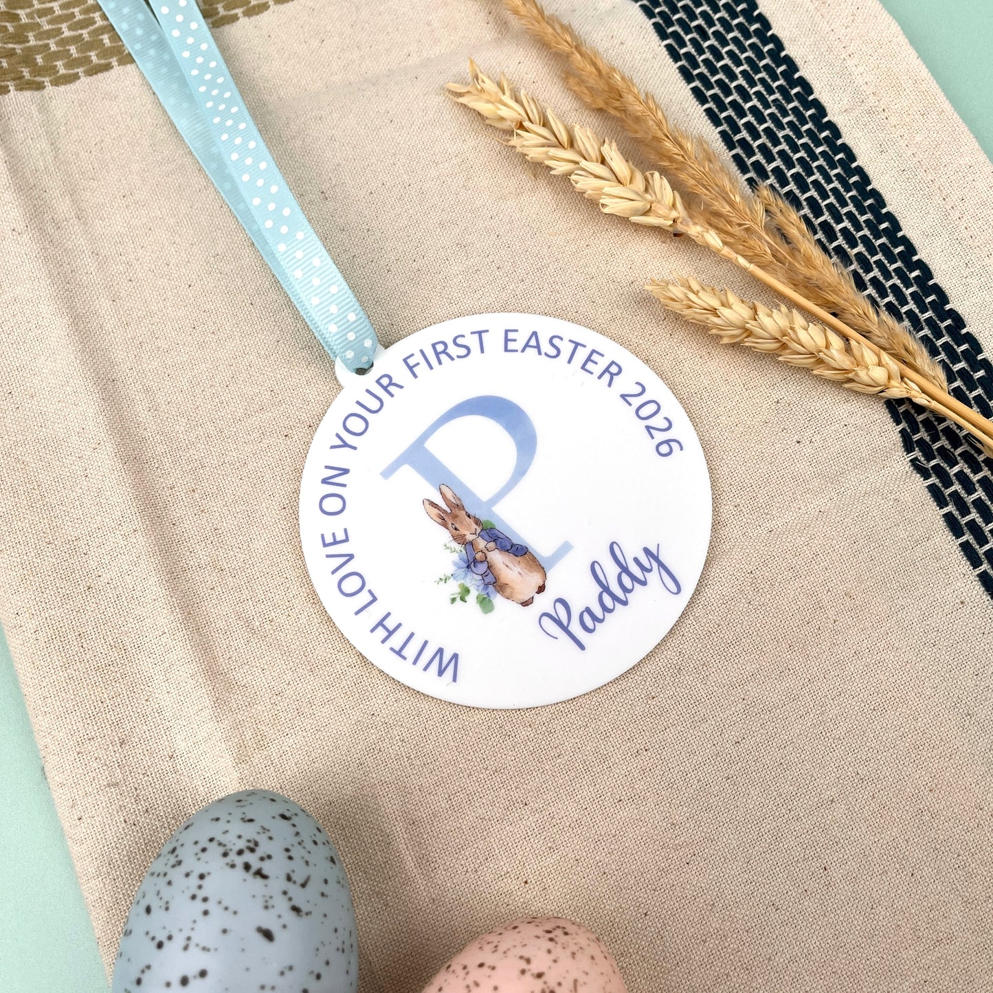 A round baby's Easter Keepsake Decoration with Personalised name and wording, illustrated with a watercolour of peter rabbit. 'with love on your first easter 2026 paddy'