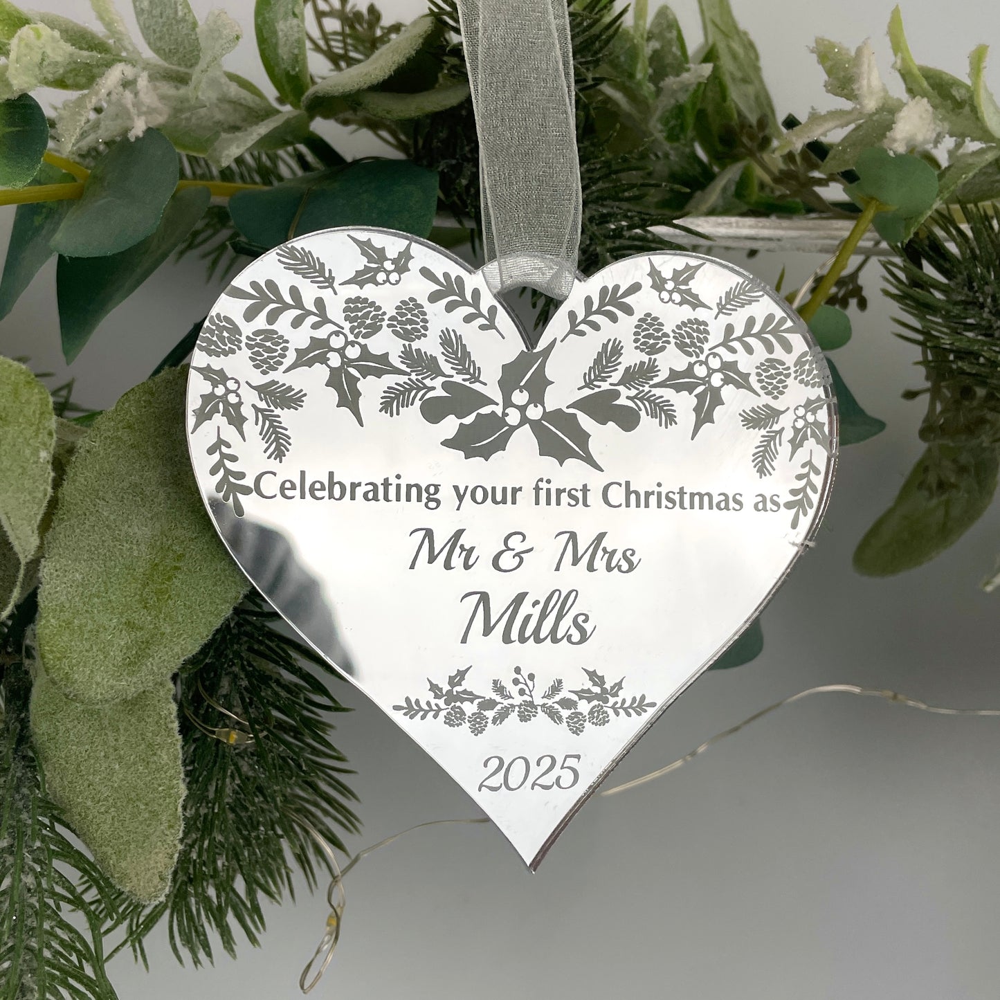 A heart-shaped, silver mirrored acrylic decoration with a winter pattern, personalized with engraved text including names and a date.