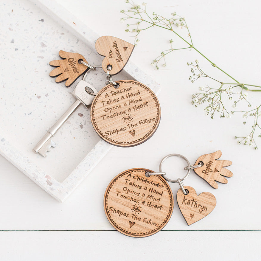 two personalised wooden teacher gift keyring with one heart and hand charm on white stone with flowers on the left and one on the right