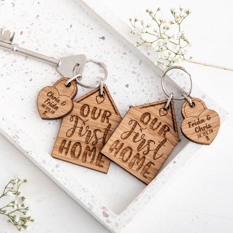 Two engraved new home keyrings with padlock charms stating names and dates, sat on a white stoned background with small white flowers