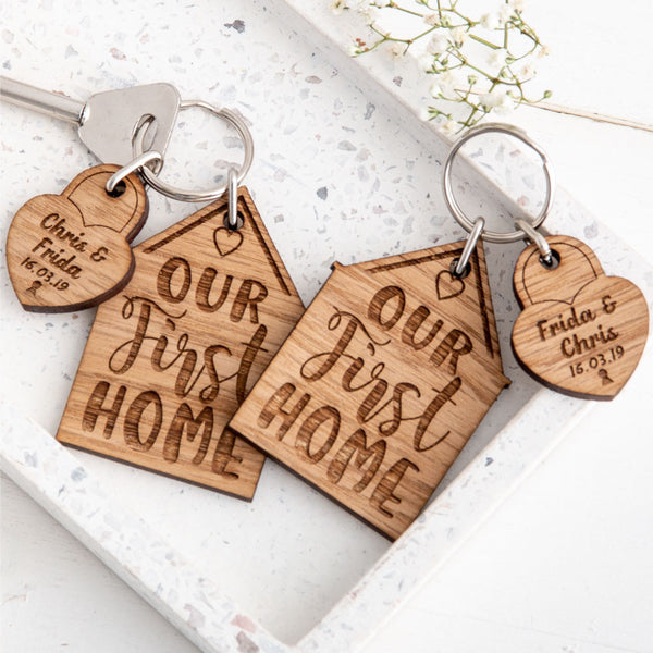 Zoomed in shot of Two engraved new home keyrings with padlock charms stating names and dates, sat on a white stoned background with small white flowers