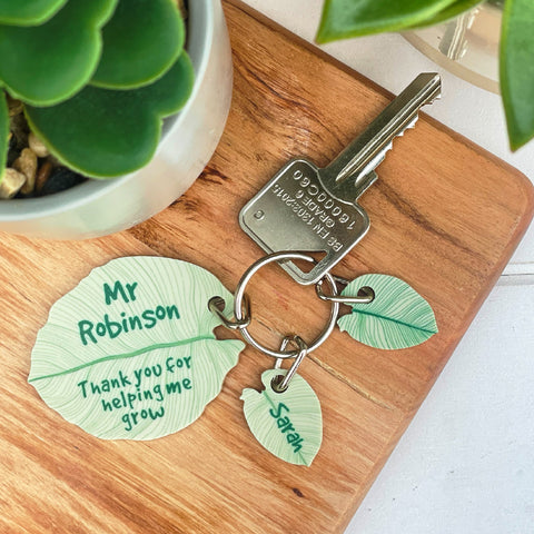 green leaf keyring personalised with Mr Robinsons two other leaf charms on a wooden background with hints of plants 