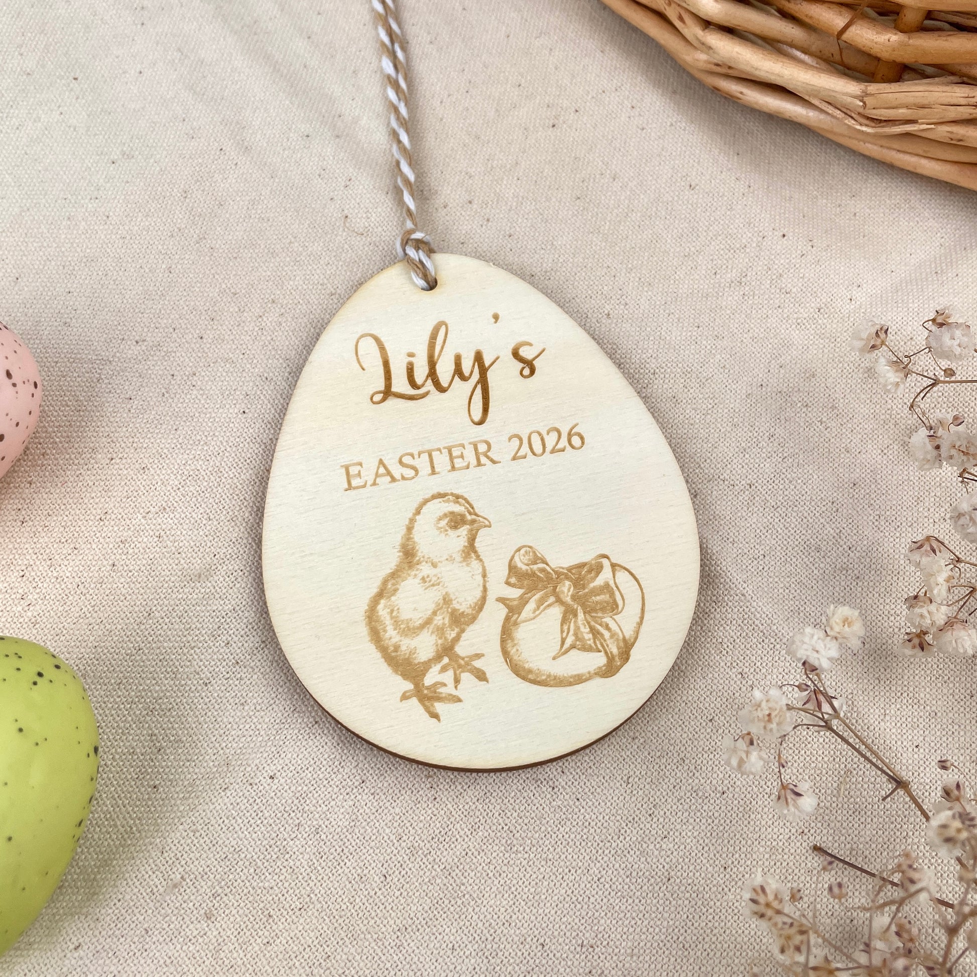 Wooden Easter egg decoration with 'Lily's Easter 2026' engraving and chick illustration, held in a hand.