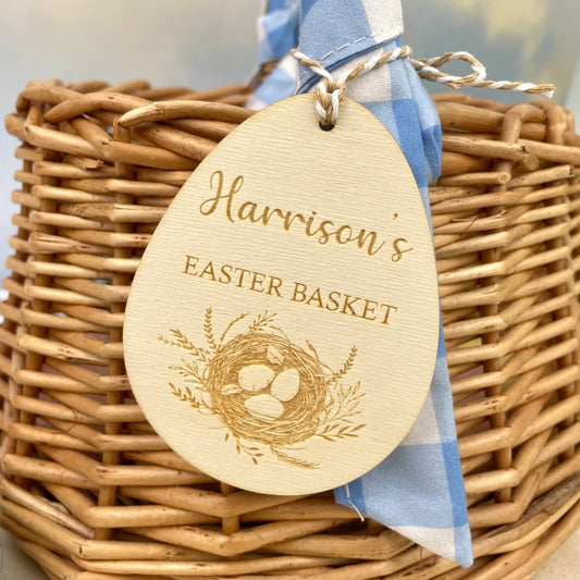 Easter egg shaped personalised wooden decoration with a beige and white string to hang on an Easter basket. 'Harrison's Easter Basket' engraved alongside a Easter nest design. 