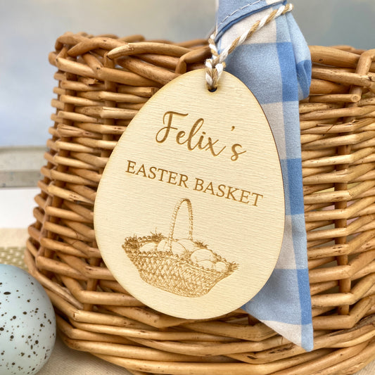 Easter egg shaped personalised wooden decoration with a beige and white string to hang from an easter basket. 'Felix's Easter Basket' engraved alongside an Easter basket design. 