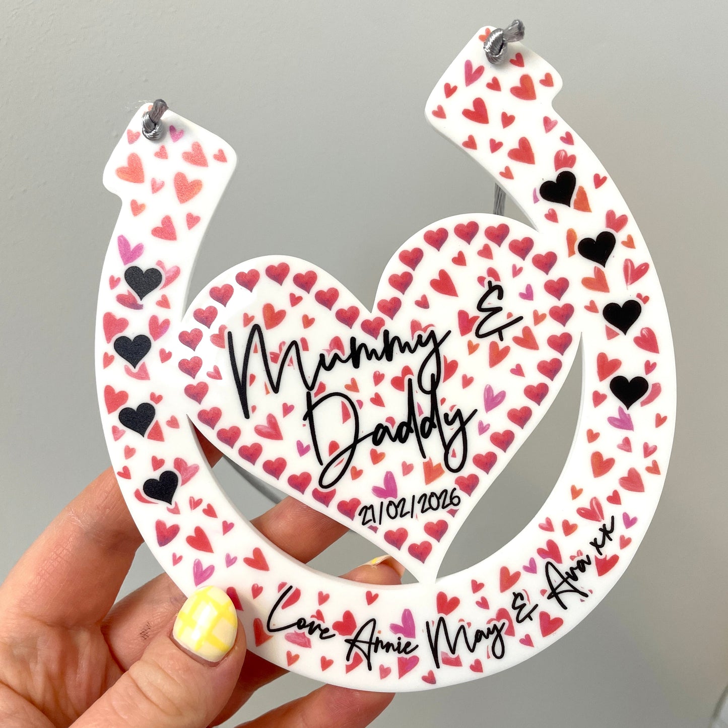 Love heart horseshoe design with printed names being held up by hands with a floral background front shot