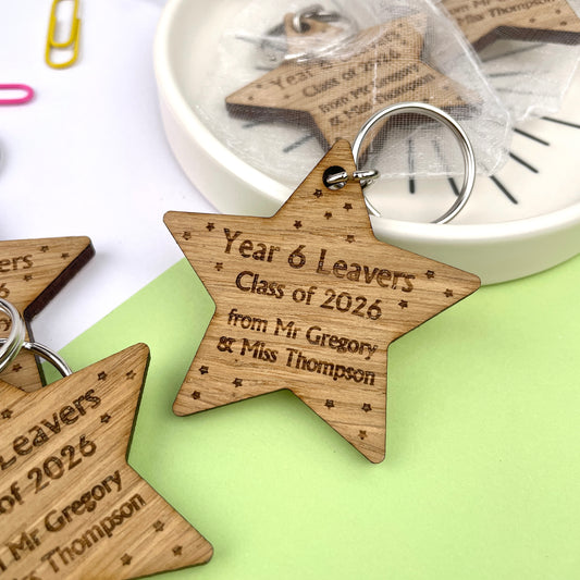 A wooden star-shaped keyring with engraved text celebrating 'Year 6 Leavers' and 'Class of 2026', along with the names of the school and teacher.