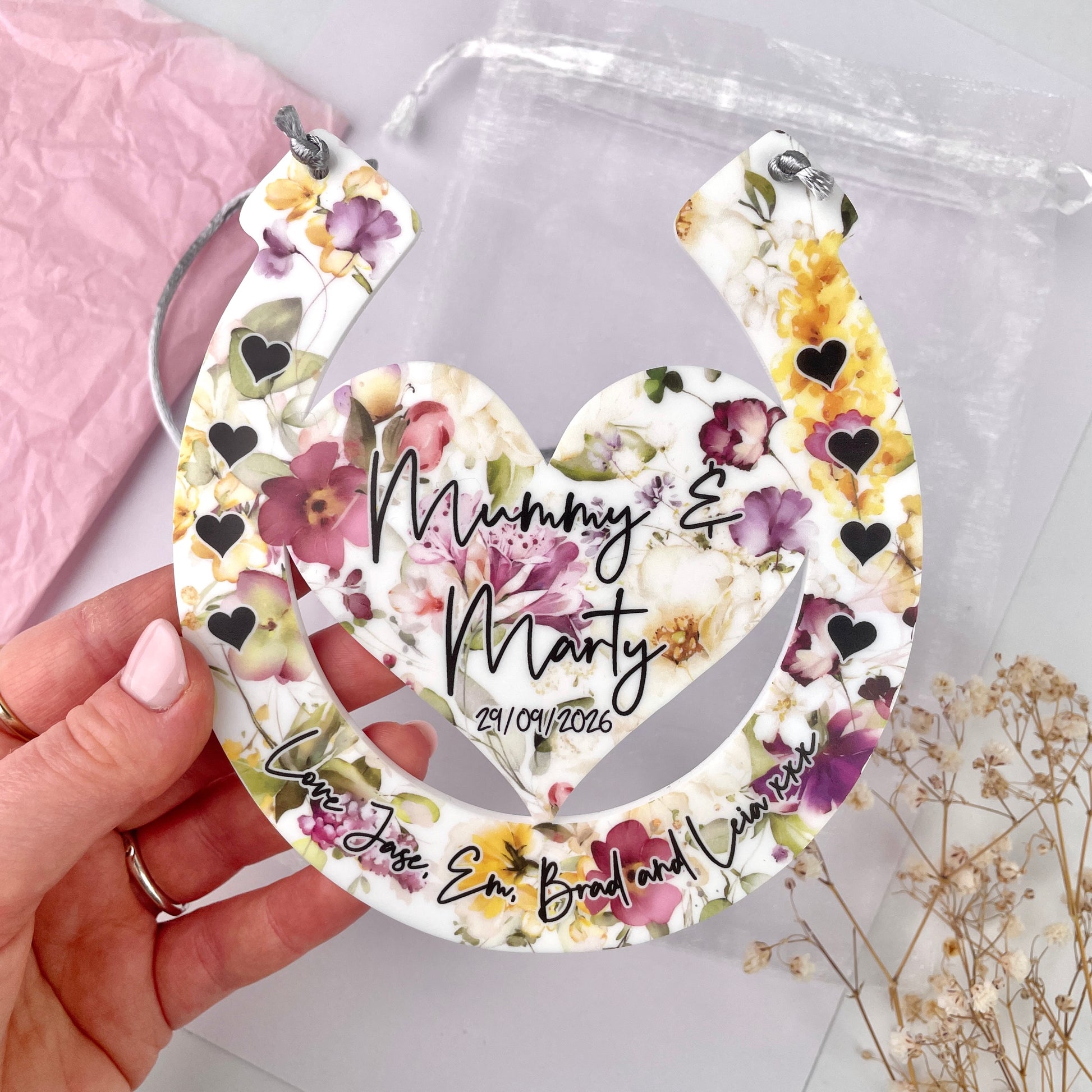 Floral horseshoe design with printed names being held up by hands with a floral background front shot 