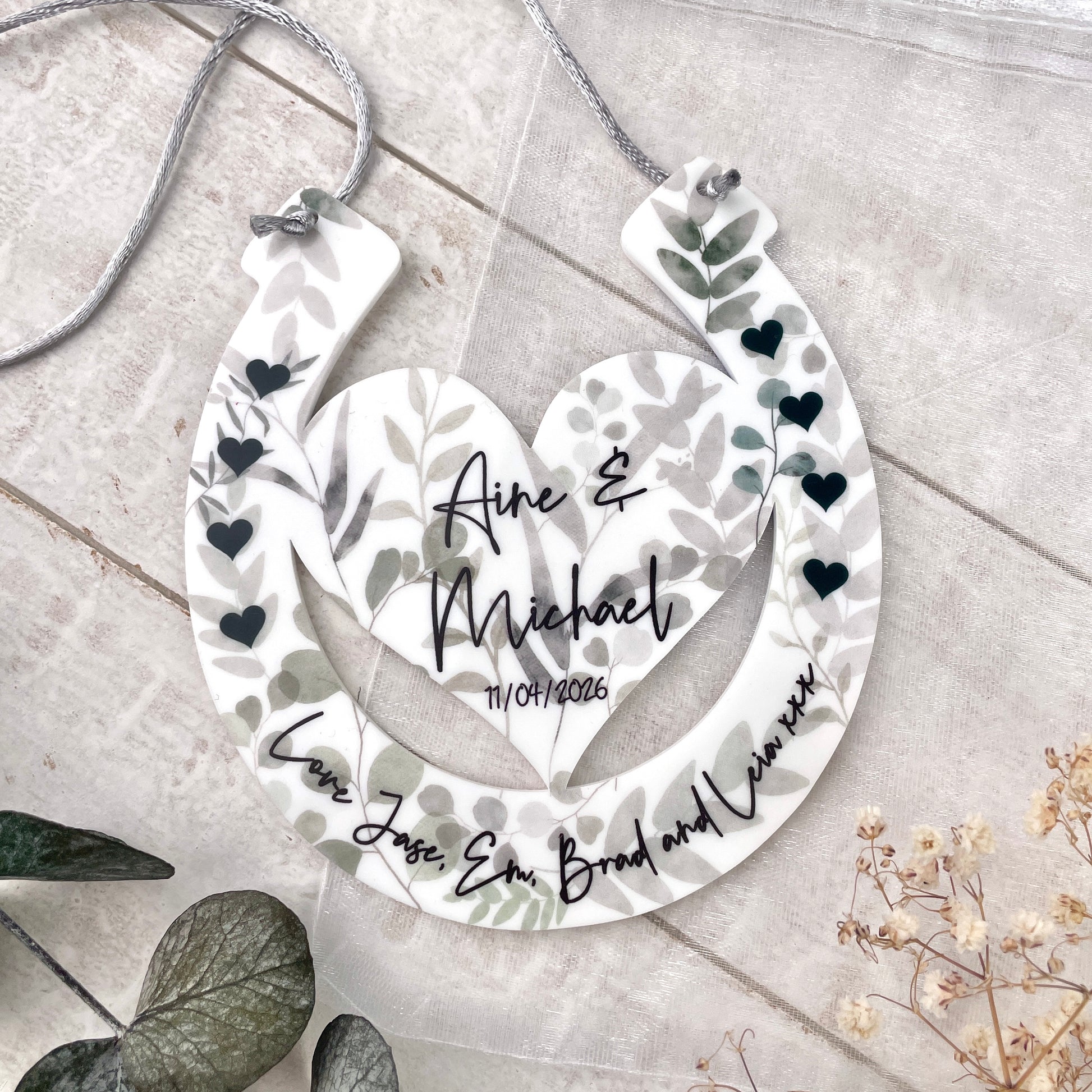 Eucalyptus design horseshoe design with printed names being held up by hands with a floral background front shot