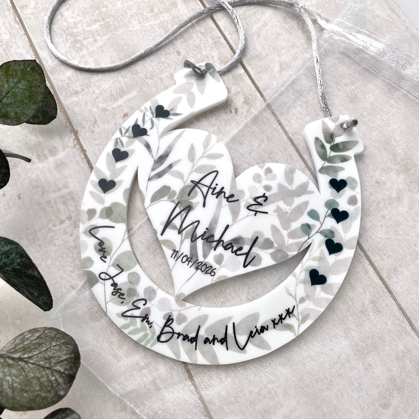 Eucalyptus design horseshoe design with printed names being held up by hands with a floral background front shot
