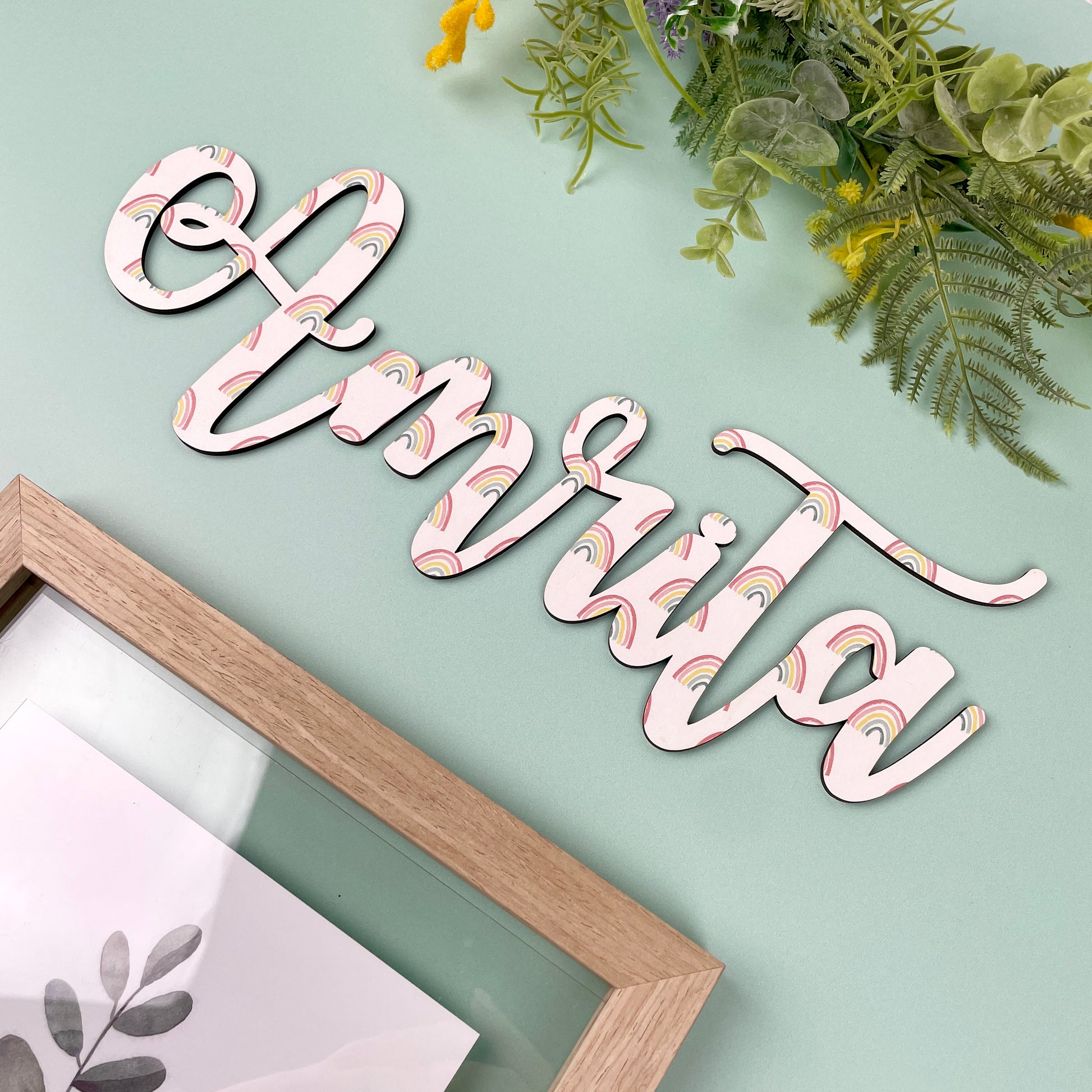 Decorative wooden name plate with 'Amrita' on a light green background with foliage