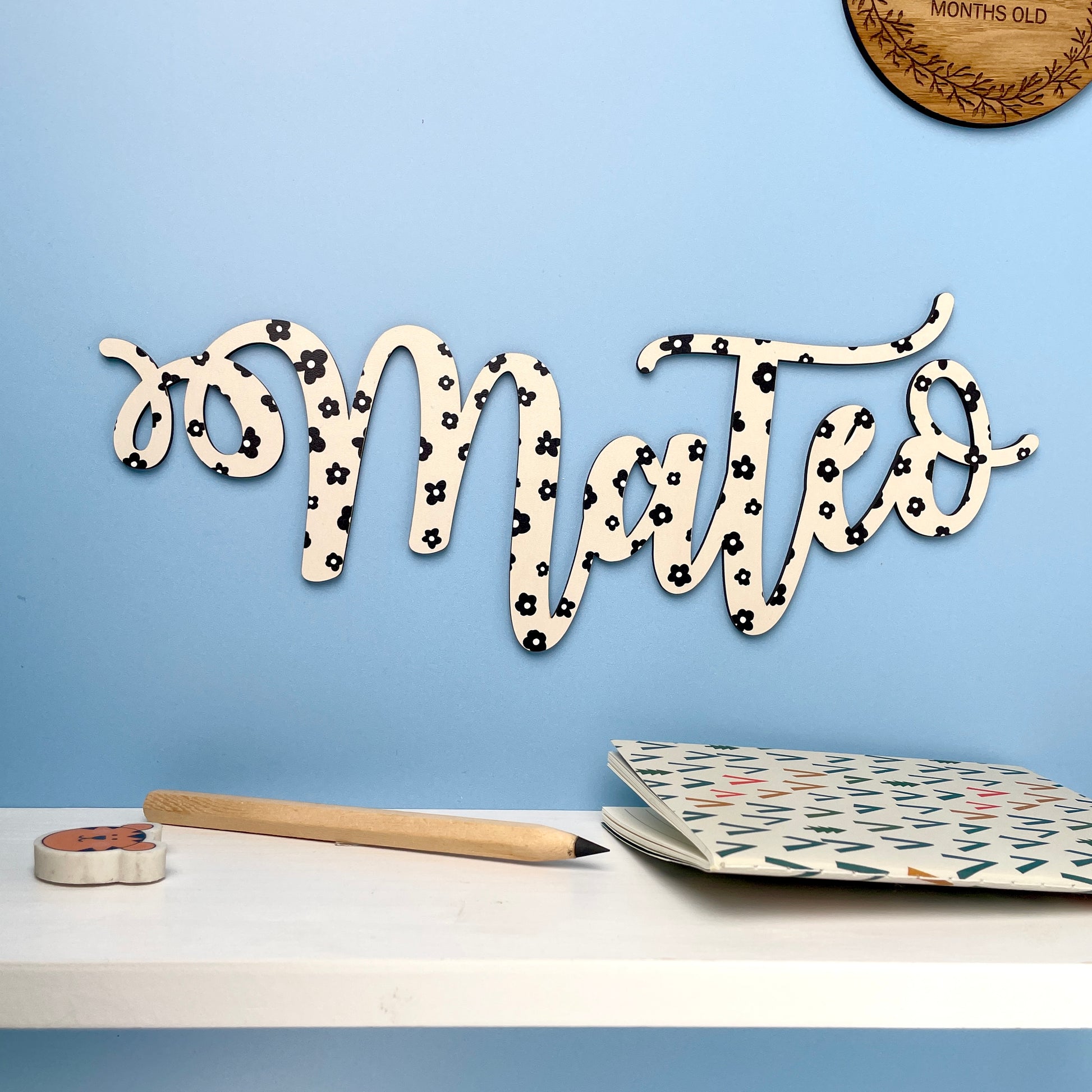 Wooden name sign with decorative elements on a desk against a blue wall.