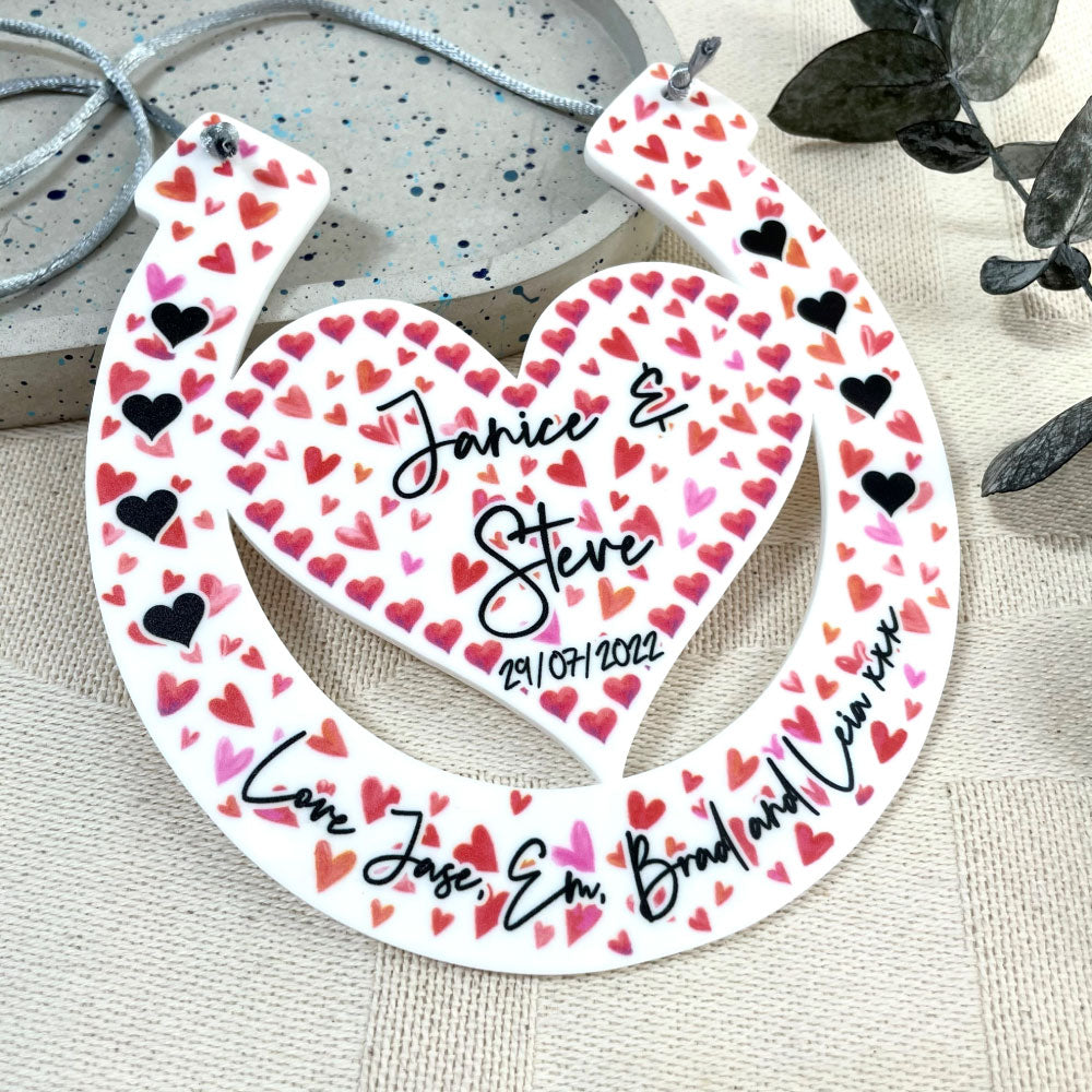 Love heart horseshoe design with engraved names being held up by hands with a floral background angled shot