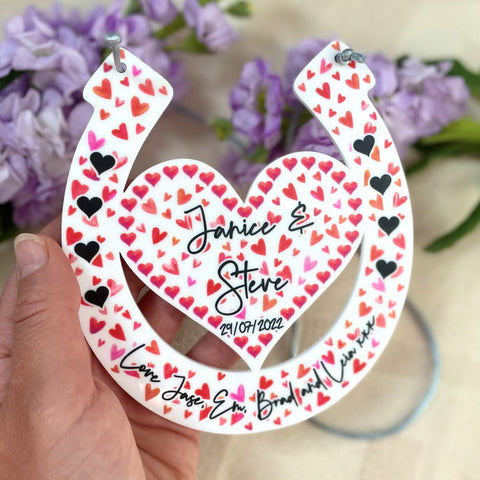 Love heart horseshoe design with engraved names being held up by hands with a floral background front shot