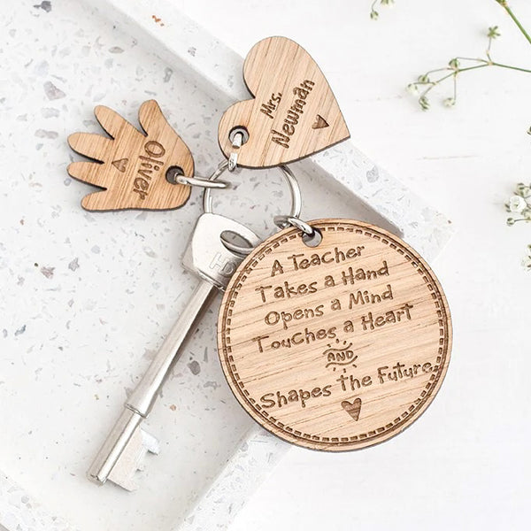 close up of personalised wooden teacher gift keyring with one heart and hand charm on white stone with flowers