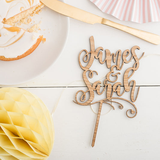 personalised cake topper with the two names james and sarah, on a white background next to cake and party decorations 